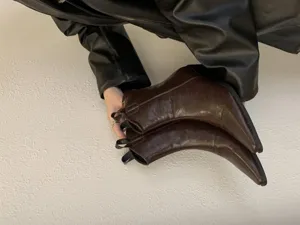 Detailed view of women brown pointed toe chunky heel western cowboy boots held by hand.