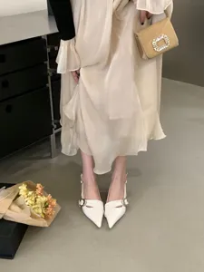 Detail view of elegant white pointed slingback heels and cream dress in a stylish indoor setting.