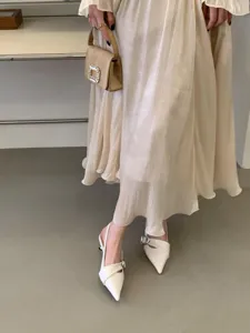 Close-up detail of stylish women's pleated midi skirt and elegant pointed-toe high heels.
