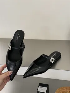 Détail de mules plates noires pointues avec bride à boucle en strass et cuir verni.