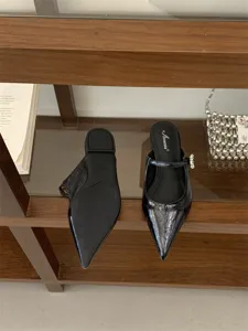 Mules plates noires à bout pointu avec détail de bride strassée, semelle et logo de la marque.