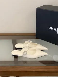Gros plan de mules plates blanches à bout pointu ornées d'une boucle en cristal étincelante.