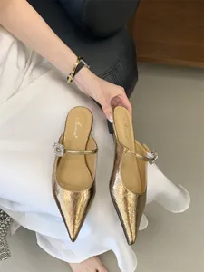 Gros plan de mules plates dorées métalliques à bout pointu avec élégante boucle en cristal.