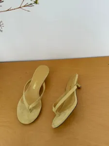 Close-up detail shot of minimalist yellow suede thong kitten heel sandals for summer wear.