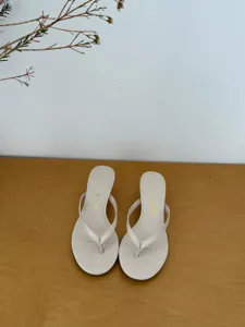 Detail view of stylish beige high heel thong sandals, minimalist wooden table scene display.