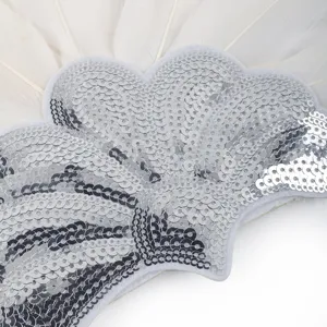Gros plan détaillé de la décoration de coiffe en plume blanche et sequins argentés.