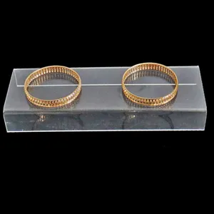 Vue détaillée de deux élégants bracelets joncs dorés avec motif ajouré sur support en acrylique.