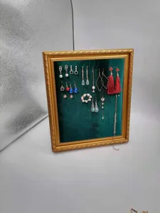 Detail shot of dark green velvet jewelry display board with gold frame and hanging earrings.