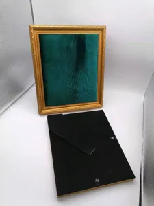 Close-up detail of the vintage dark green velvet jewelry display frame with gold edge.