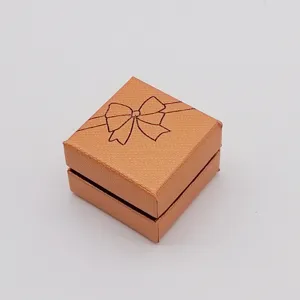 Orange square jewelry gift box detail, textured paper material with bow ribbon print closeup.