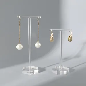 Élégantes boucles d'oreilles en perle et métal sur supports en acrylique transparent.