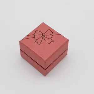 Pink square jewelry gift box detail, textured surface with cute black bow print design.
