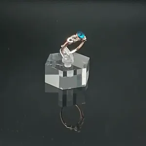 Gros plan détaillé de la bague en or rose avec une pierre bleue étincelante sur support.