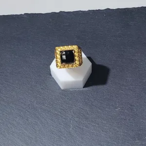Gros plan détaillé d'une bague carrée dorée avec pierre noire sur un support blanc