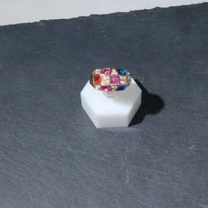 Élégant bague en pierres précieuses multicolores sur support hexagonal blanc pour vitrine de bijoux.