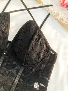 Close-up of black lace bodysuit detail, featuring delicate floral hollow-out pattern and thin straps.