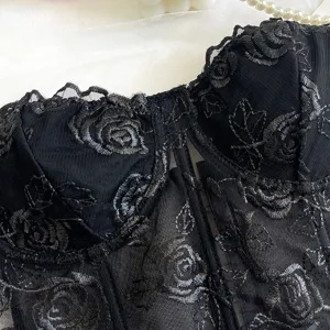 Primo piano del top corsetto in rete di pizzo nero con elegante ricamo di rose e dettagli.