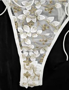 Dettaglio in primo piano di lingerie in rete trasparente con ricamo floreale oro e bianco.