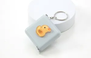 Detalle en primer plano del mini flexómetro gris con bonito adorno de patito amarillo.