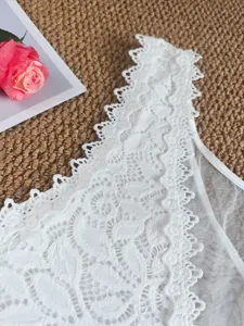 Détail en gros plan d'un body caraco en dentelle blanche avec bordure florale et résille fine.