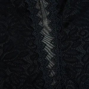 Gros plan sur un tissu de dentelle noire, motif floral et bande texturée centrale.