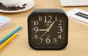 Primer plano de un despertador de cuarzo cuadrado negro minimalista con números blancos.
