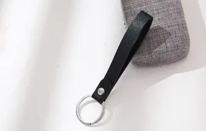 Detailfoto van een zwarte lederen sleutelhanger met metalen ring en drukknoop voor sleutels.