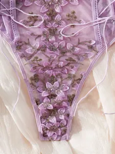 Primo piano di un bellissimo body sexy in rete viola ricamato a fiori con delicati lacci sottili.