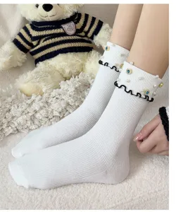 Detailed close-up view of white mid-tube socks with pearls, rhinestones and black ruffles.