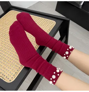 Close up view of red ribbed socks featuring elegant pearl and rhinestone embellished cuffs.