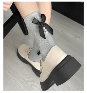 Close-up detail shot of grey knit socks featuring an elegant black bow and faux pearls.