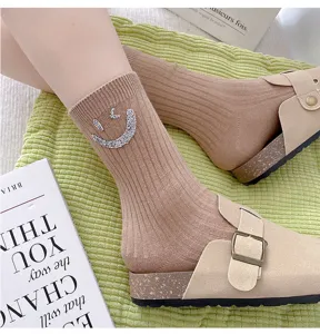 Detailed close-up of beige ribbed knit mid-tube socks decorated with sparkling rhinestone smiley.