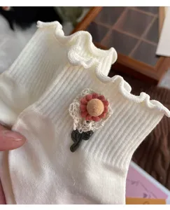 Close-up detail of white ruffle socks featuring cute 3D floral patch and ribbed knit.