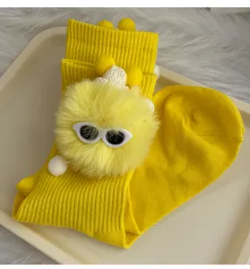 Close-up of cute yellow mid-tube socks featuring a fluffy pom-pom doll with sunglasses.