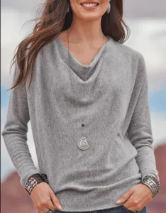 Close-up detail of grey cowl neck long sleeve knit top with elegant pendant necklace.