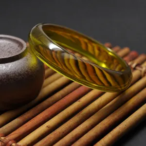 Close-up view of a transparent green synthetic amber resin bangle bracelet on bamboo mat.