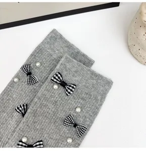 Close-up detail of gray knitted socks with cute plaid bows and pearl decorations.