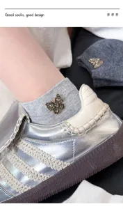 Detail shot of grey cotton socks featuring a sparkling rhinestone butterfly and silver sneakers.