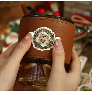 Detailansicht eines Glasbechers mit brauner Lederhülle und süßem Weihnachtsfuchs-Aufkleber.