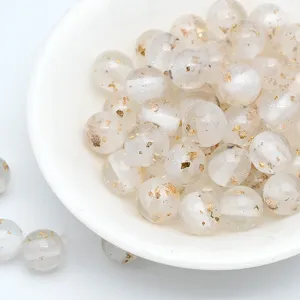 Close-up detail shot of translucent resin beads filled with shiny gold foil flakes for DIY crafts.