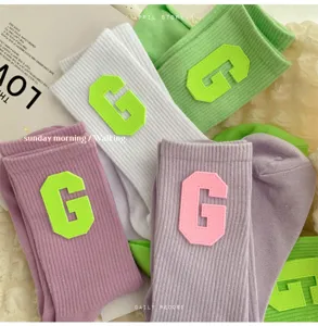 Close-up detail of ribbed cotton socks featuring contrast varsity letter G patch in trendy colors.