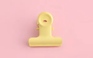 Primer plano detallado de una pinza portapapeles de metal amarillo pastel sobre fondo rosa.
