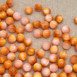 Primo piano di perline in resina rosa e oro, materiali lisci e rotondi per la creazione di gioielli.