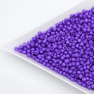 Close-up detail of vibrant purple glass seed beads displayed on a white tray, ideal for DIY crafts.
