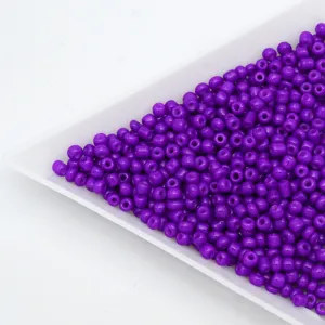 Purple glass seed beads in white tray for DIY handmade bracelets and jewelry accessories.