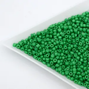 Close-up detail of green glass seed beads in a white tray, perfect for DIY jewelry making.