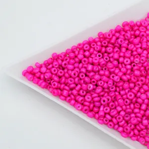 Close-up of vibrant hot pink glass seed beads in a white tray, perfect for DIY jewelry making.