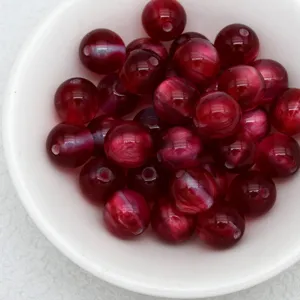 Close-up detail of deep red cat-eye beads in a white bowl, perfect for DIY jewelry making.