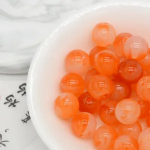Close-up detail of orange marbled acrylic beads in a white bowl, perfect for DIY jewelry crafts.