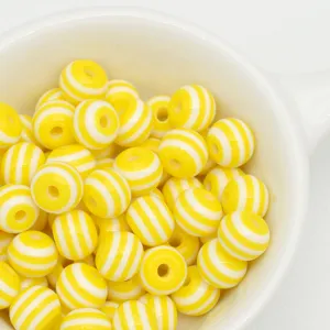 Close-up of yellow and white striped resin beads in a bowl for DIY crafts and jewelry making.